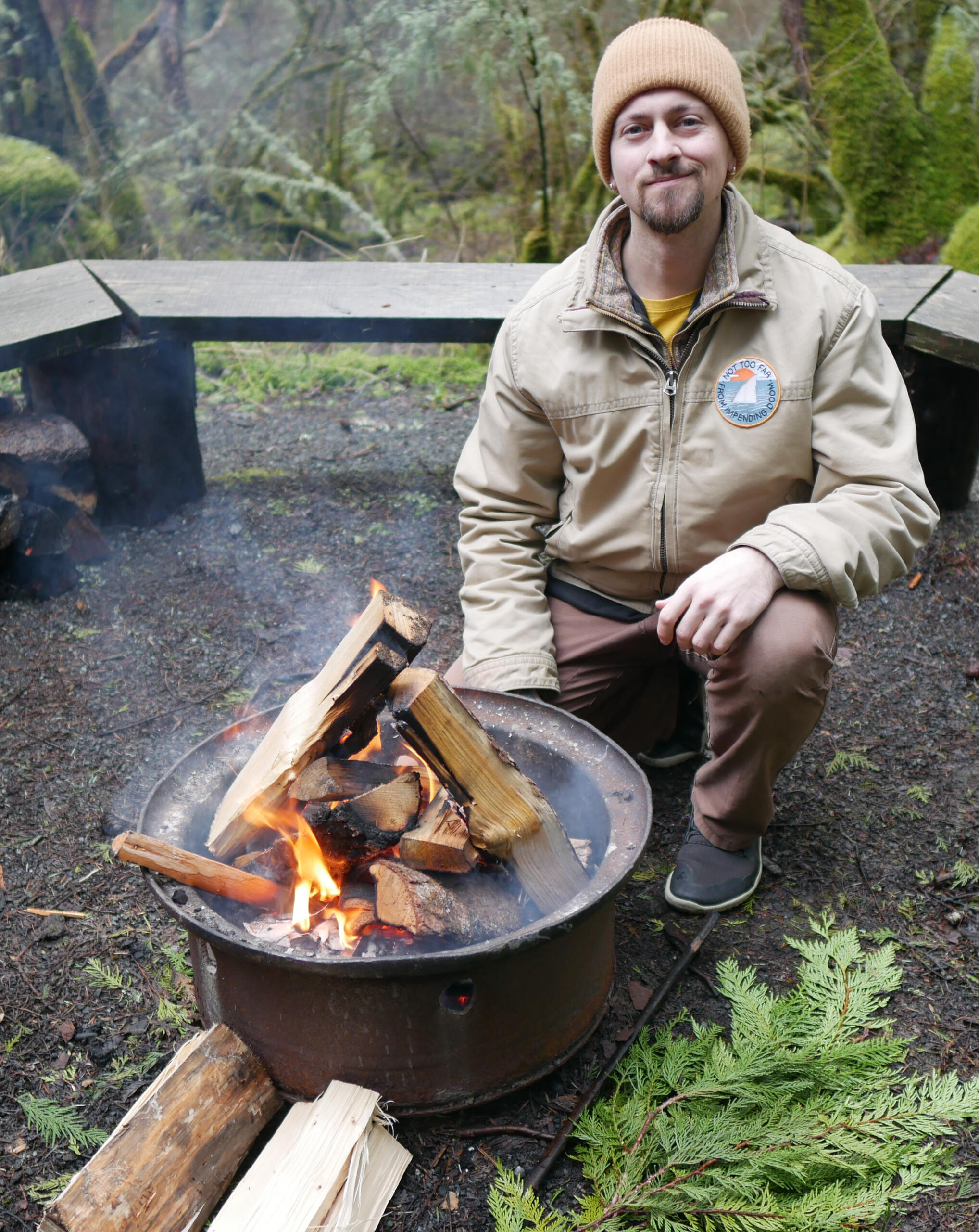 Adrian dressed warm squatting next to a small fire, with cedar boughs at his feet Adrian dressed warm squatting next to a small fire, with cedar boughs at his feet